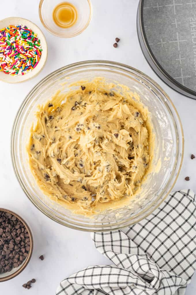 Finished chocolate chip cookie cake dough in a glass mixing bowl.