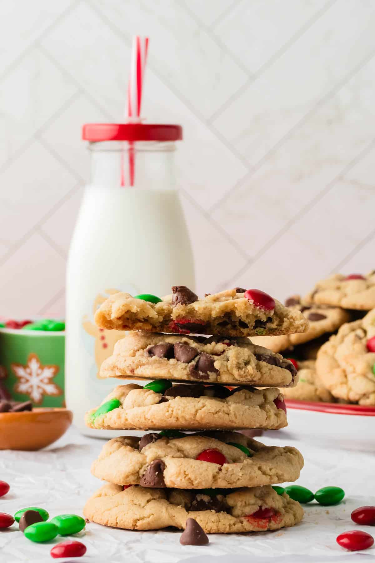 A stack of Christmas M&M cookies in front of a glass of milk.