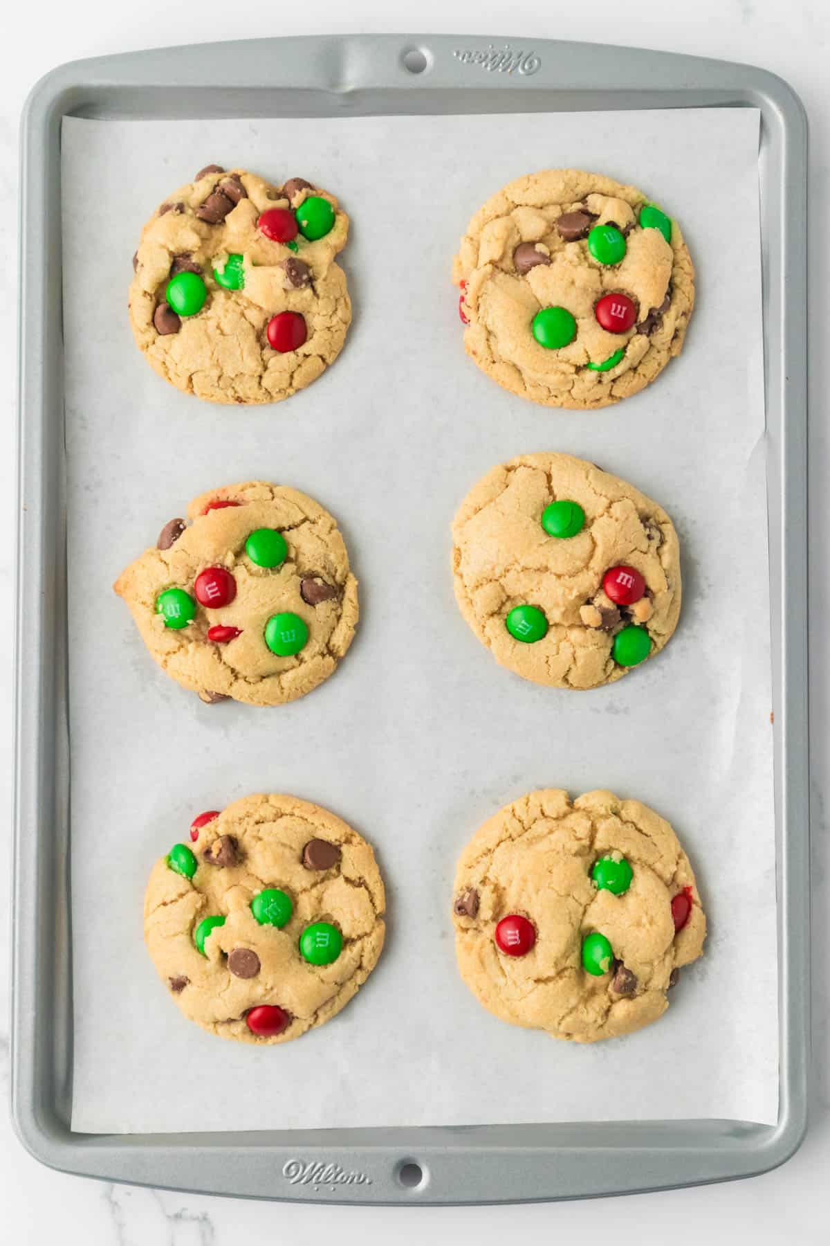 Baked Christmas M&M cookies on a baking sheet lined with parchment paper.