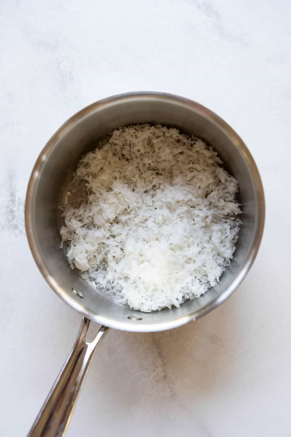 Adding sweetened coconut to a saucepan to toast it.