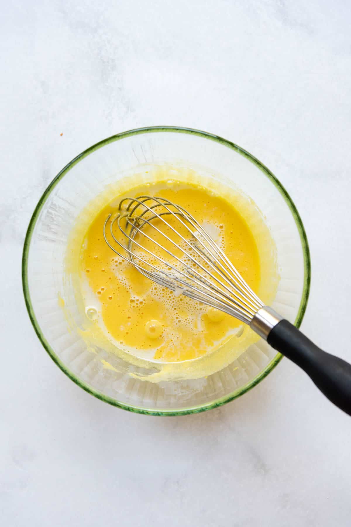 Whisking hot coconut milk and cream into egg yolks and sugar in a bowl.