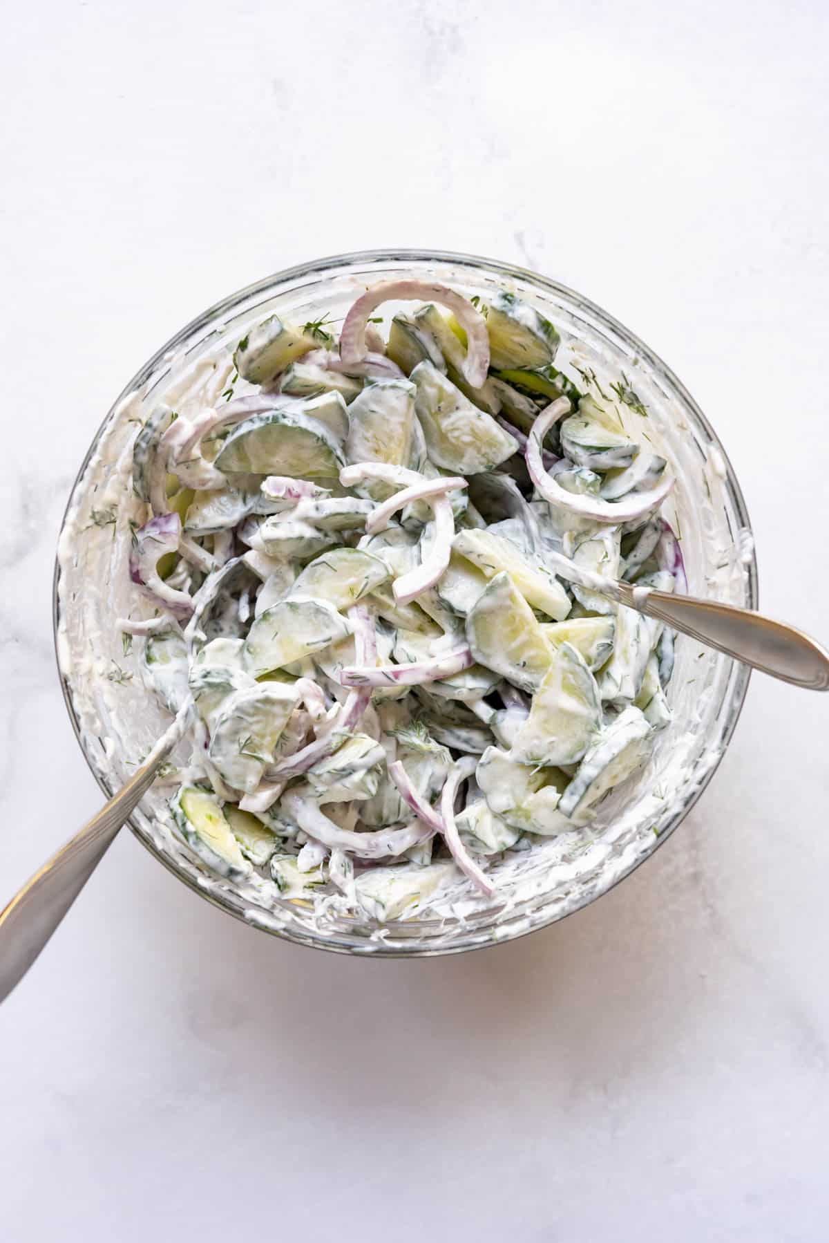 Tossing German cucumber salad ingredients together in a bowl with two spoons.