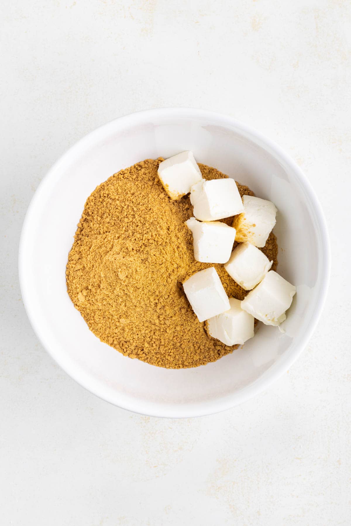 Adding softened cream cheese to finely crushed gingersnap cookie crumbs.