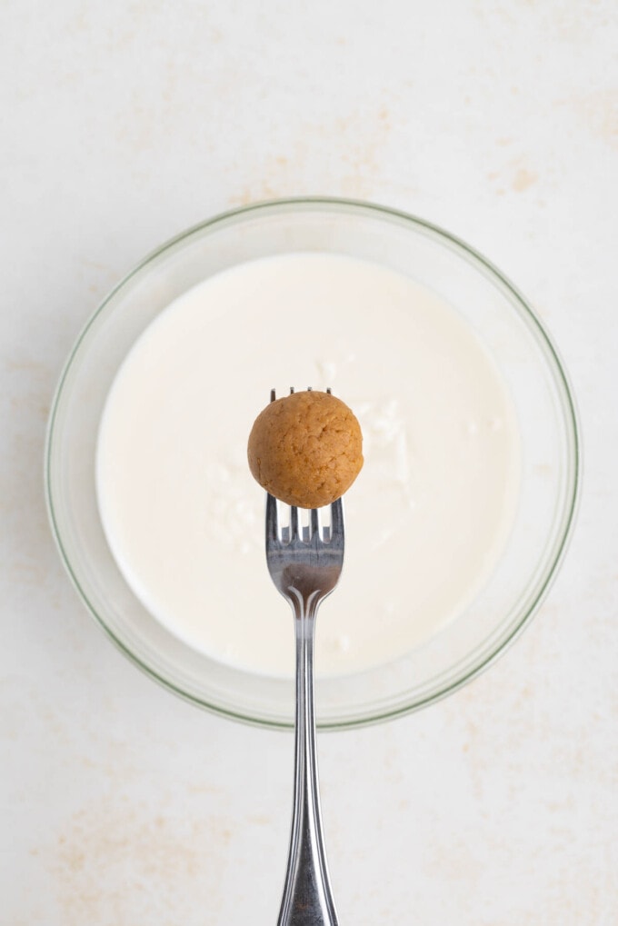 A gingerbread truffle center on a fork over a bowl of melted white chocolate.