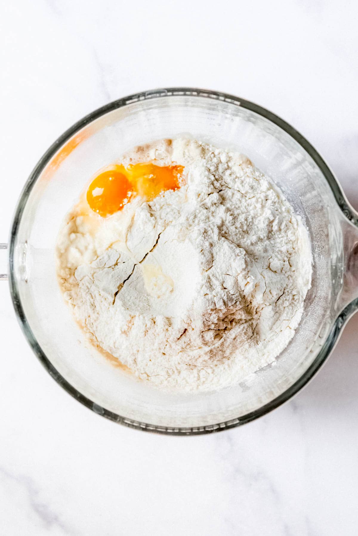 Adding flour and egg yolks to proofed yeast in a glass mixing bowl.