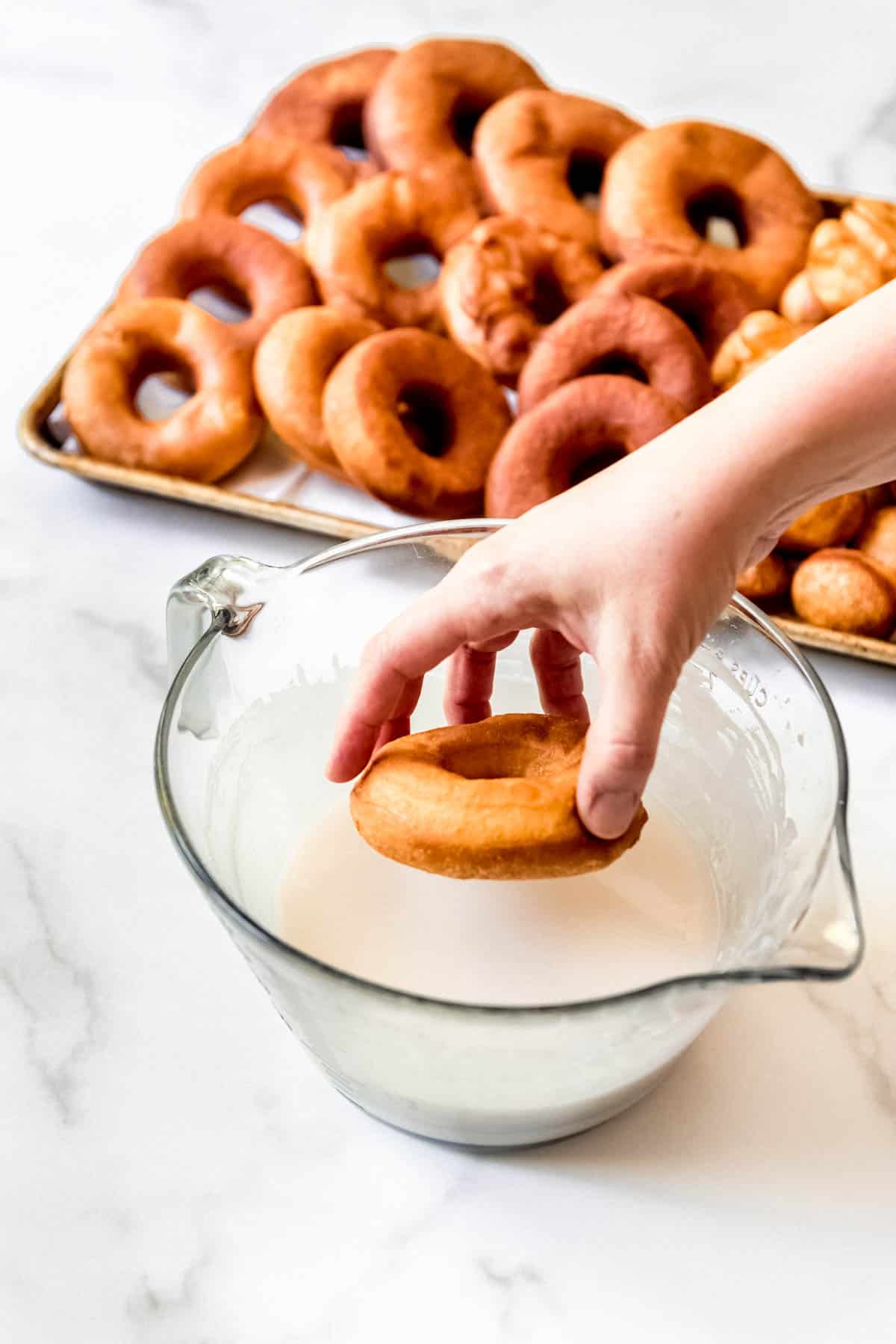 Dipping a freshly fried donut into donut glaze.