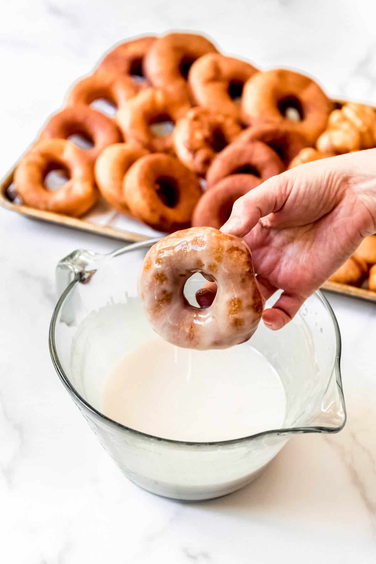 A freshly dipped glazed donut being held over the glaze.