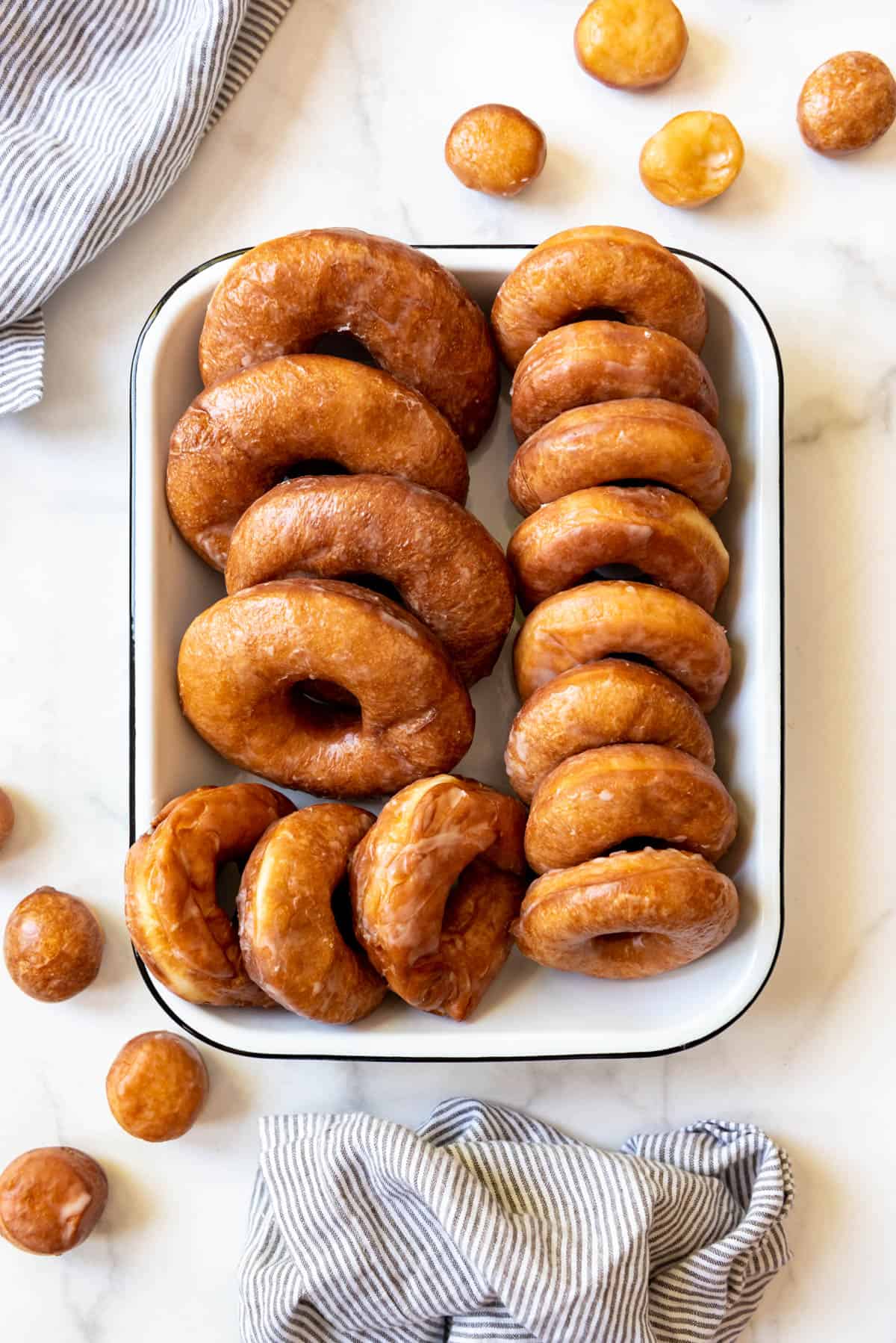 An overhead image of more than a dozen glazed donuts in a white baking dish.