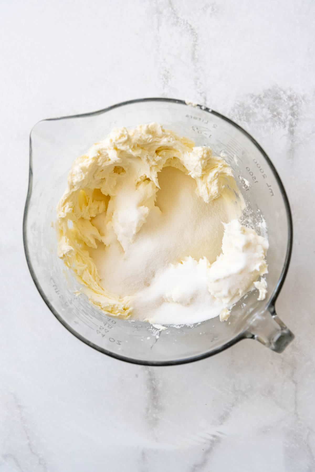 Adding granulated sugar to cream cheese in a bowl.