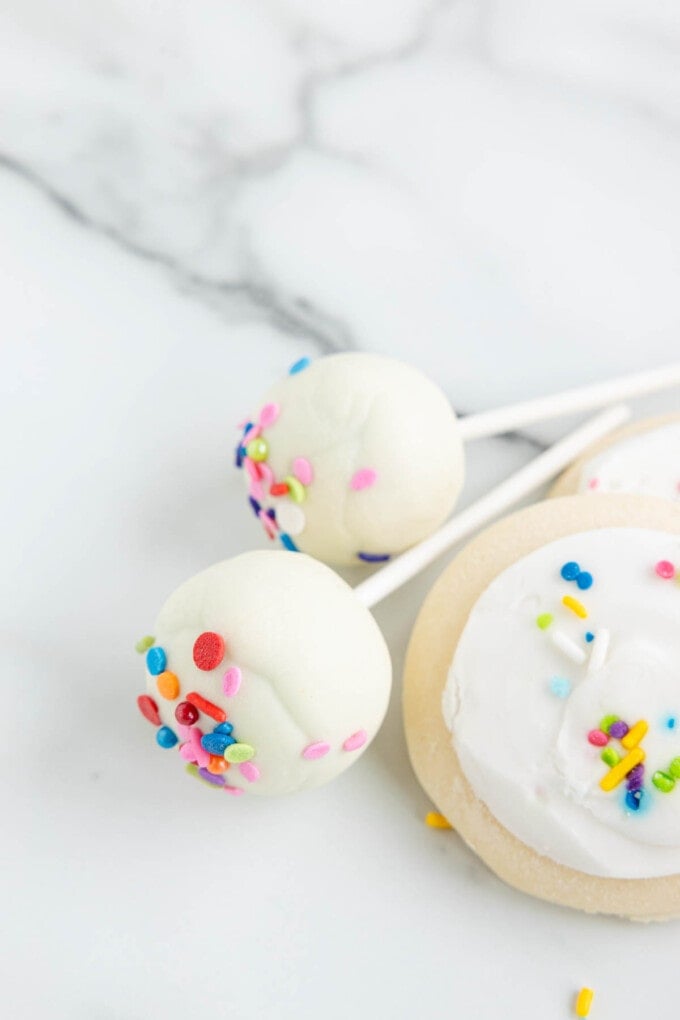 Two lofthouse cookie cake pops next to lofthouse cookies.