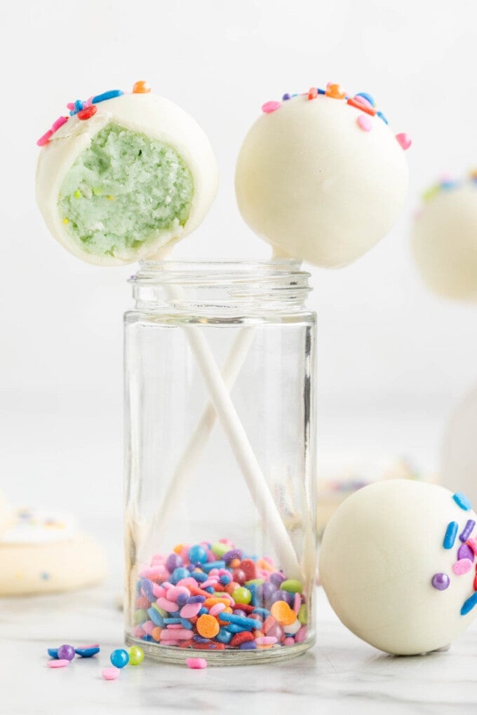 Two lofthouse cookie cake pops sticking out of ajar with a bite taken out of one of them.
