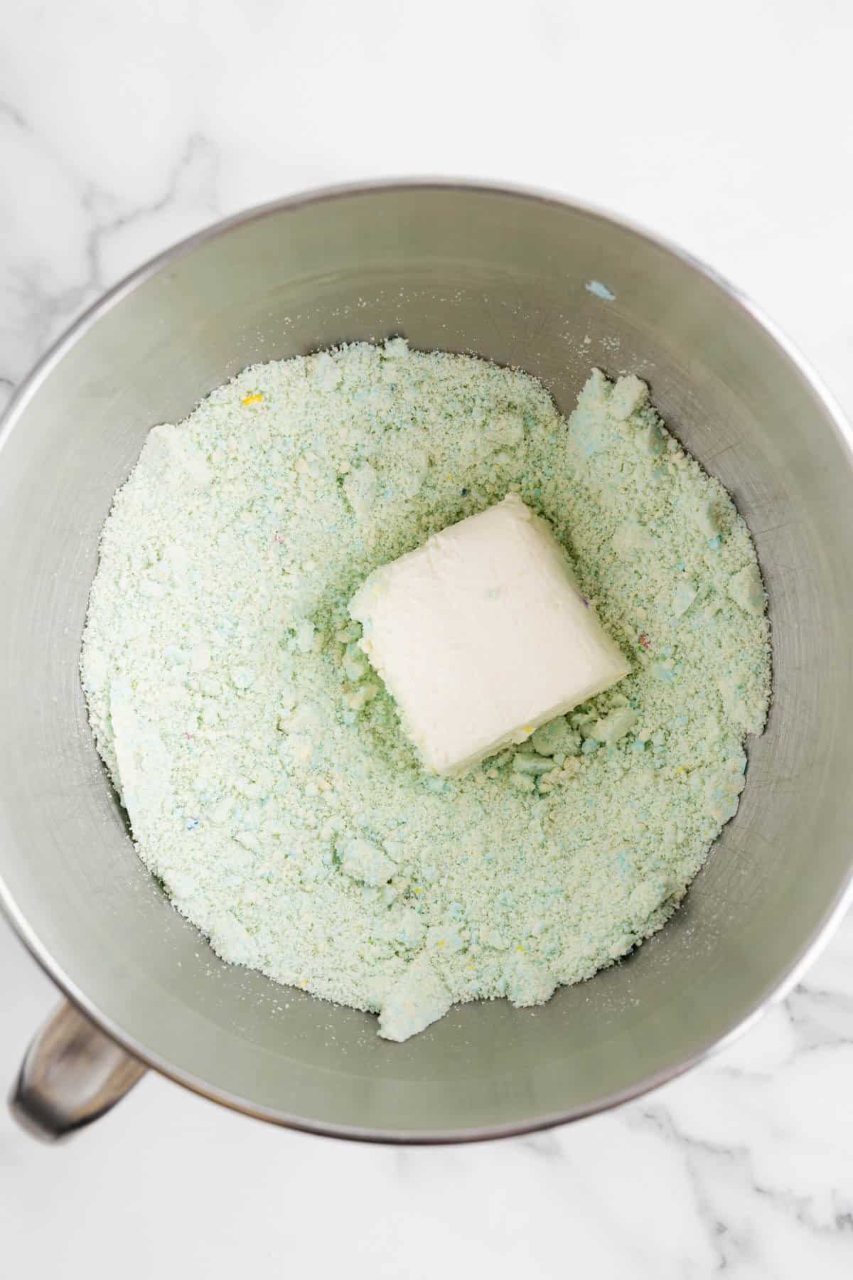 Adding softened cream cheese to crushed Lofthouse cookies in a mixing bowl.