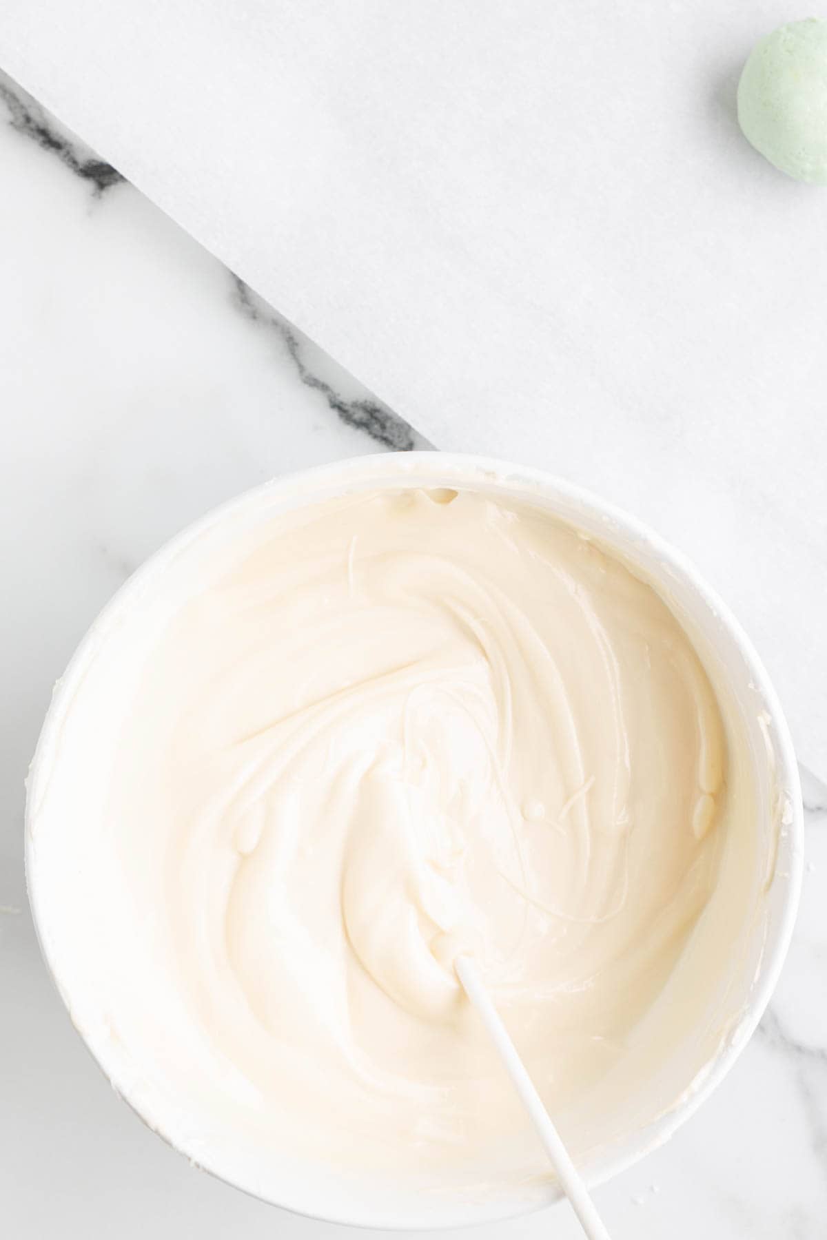 Melted white chocolate in a bowl and a treat stick being dipped into it.