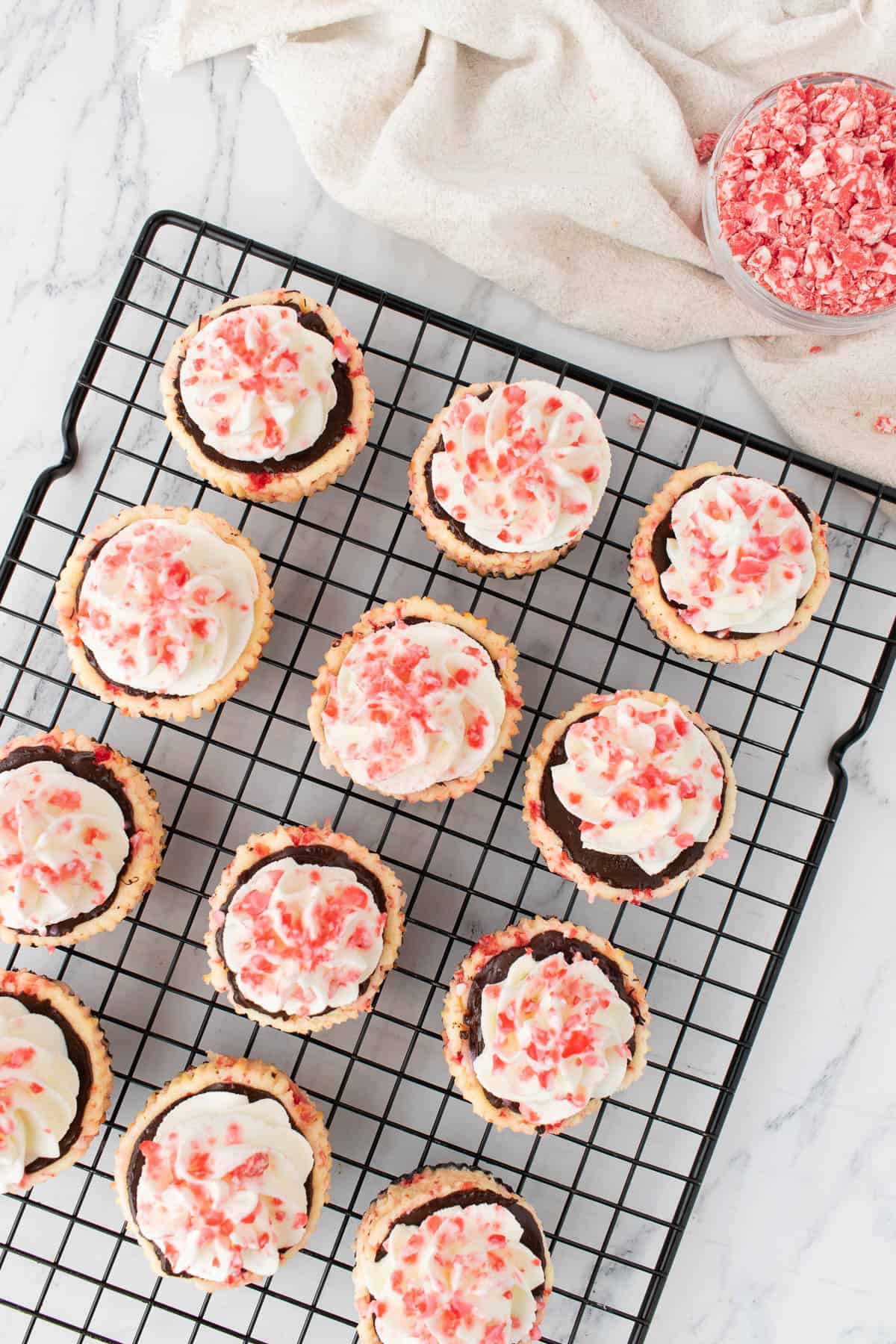 Decorated mini white chocolate peppermint cheesecakes on a black wire rack.