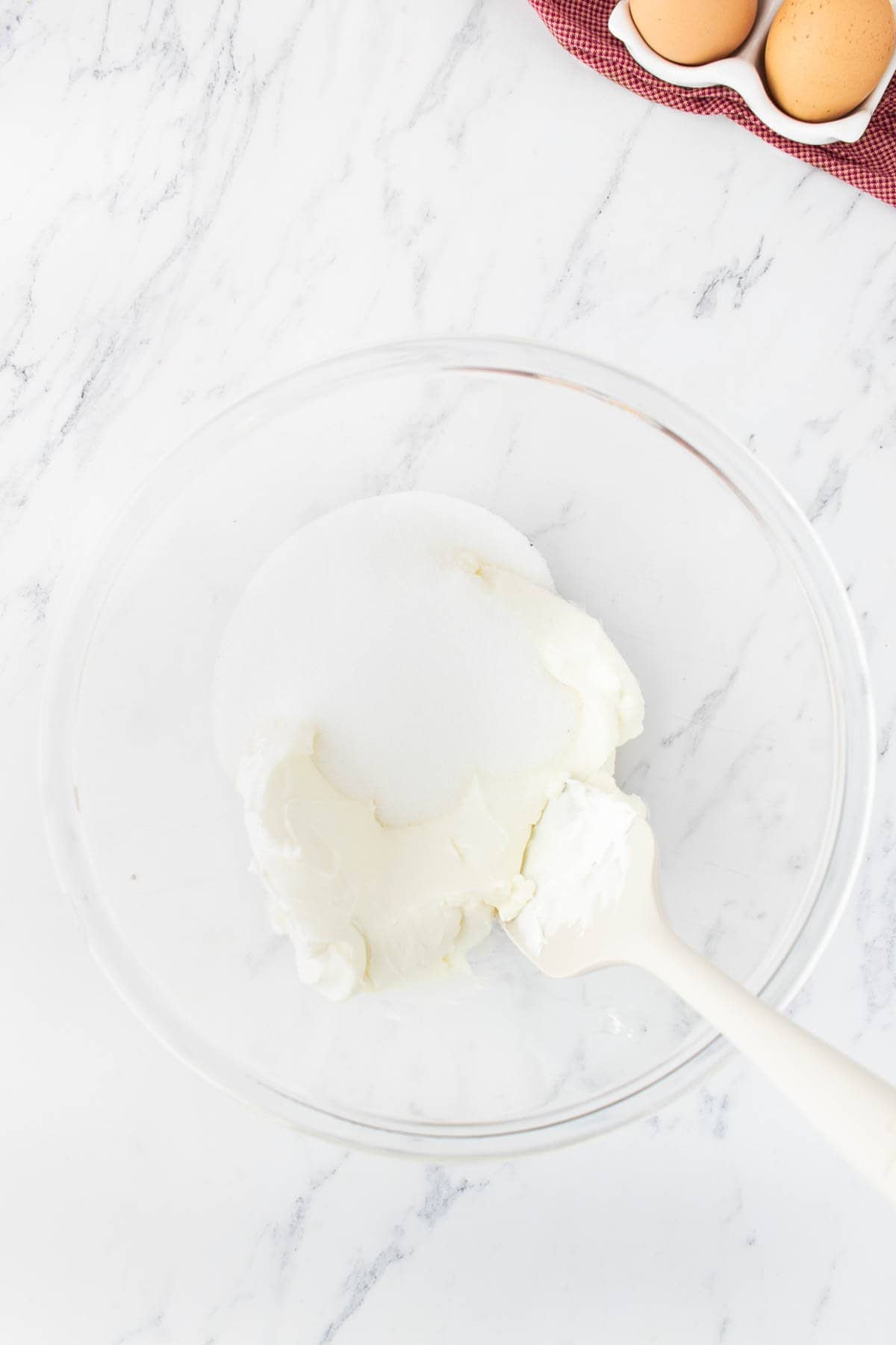 Combining softened cream cheese and granulated sugar in a large glass mixing bowl.