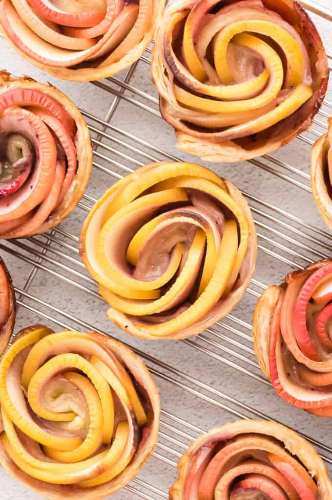 An overhead image of puff pastry apple roses on a wire rack.