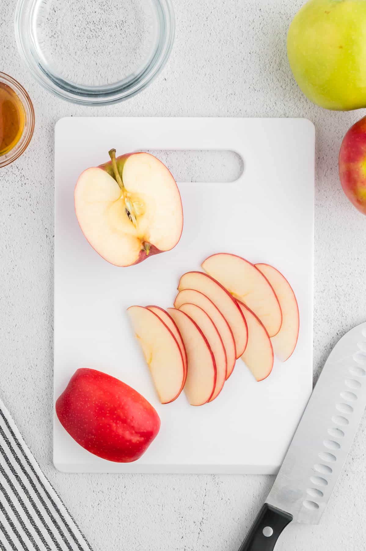 Thinly sliced apples on a white cutting board.