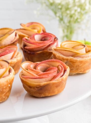 An image of puff pastry apple roses on a white cake stand.