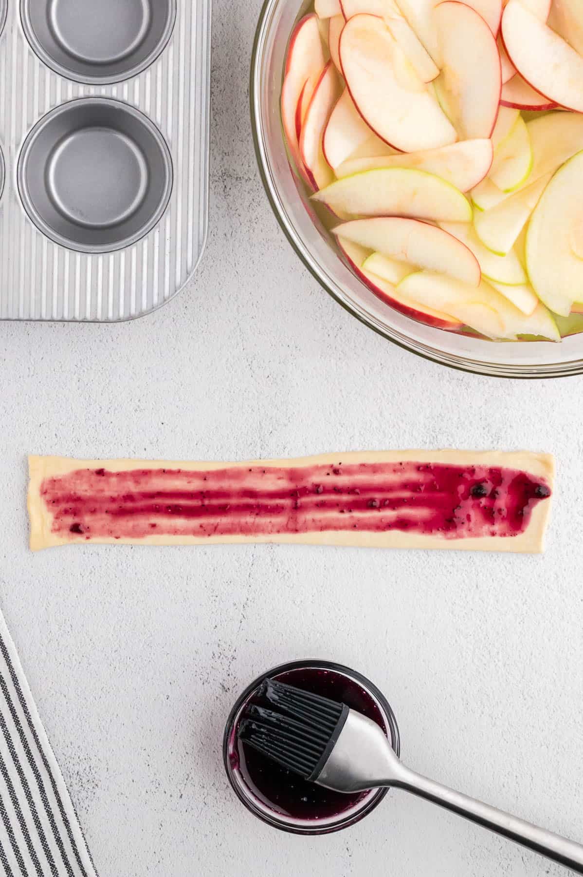 Brushing a strip of puff pastry dough with jam.