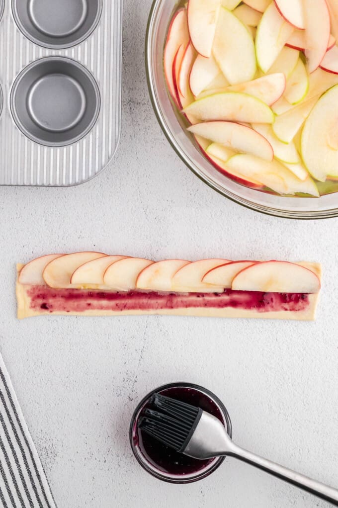 Thinly sliced apples arranged in an overlapping row on a strip of puff pastry brushed with jam.