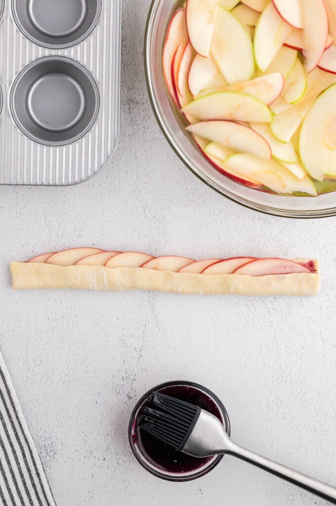 Folding puff pastry up over thinly sliced apples that have been arranged in rows.