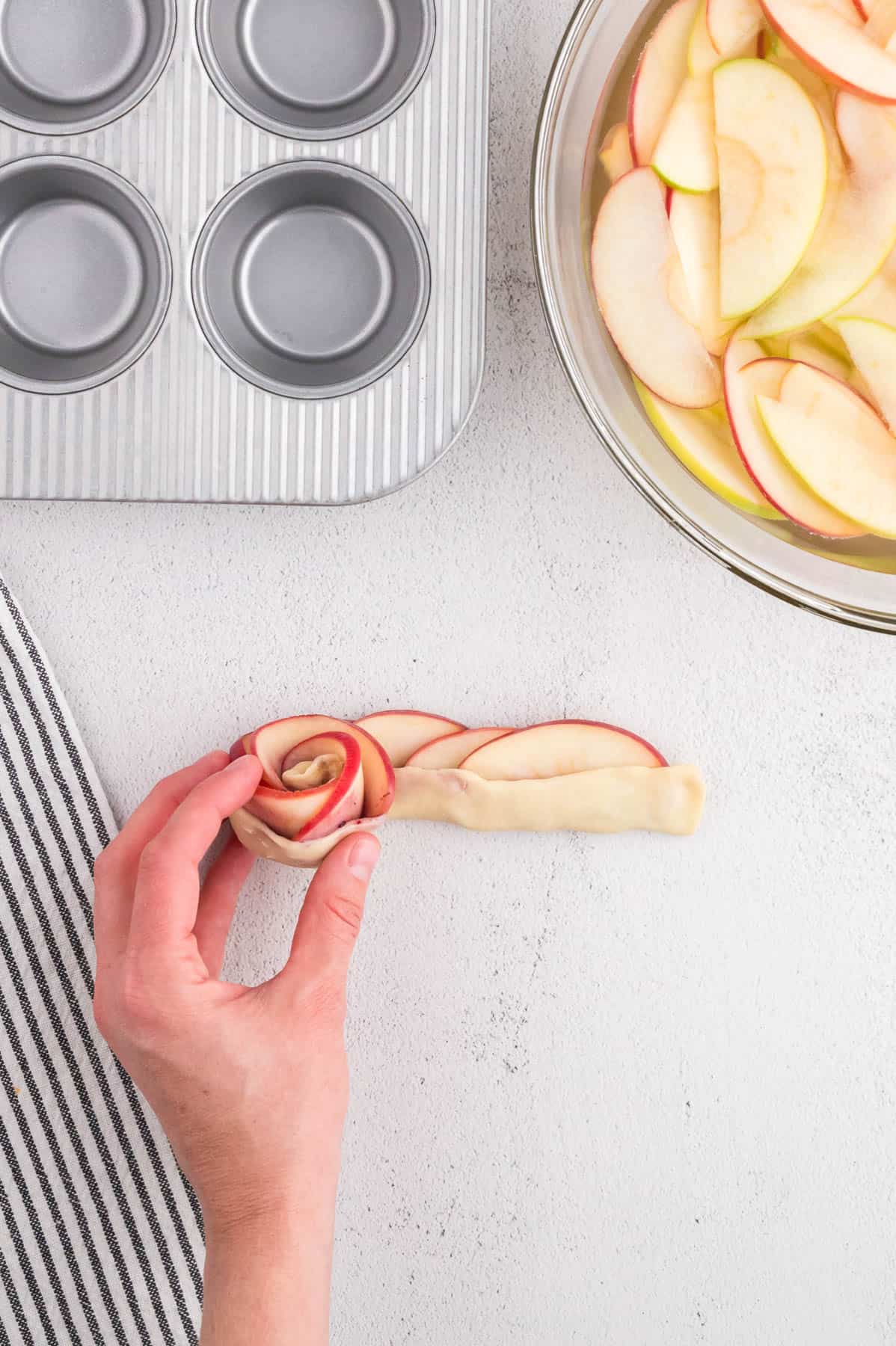 Rolling up apples and puff pastry into a flower shape.