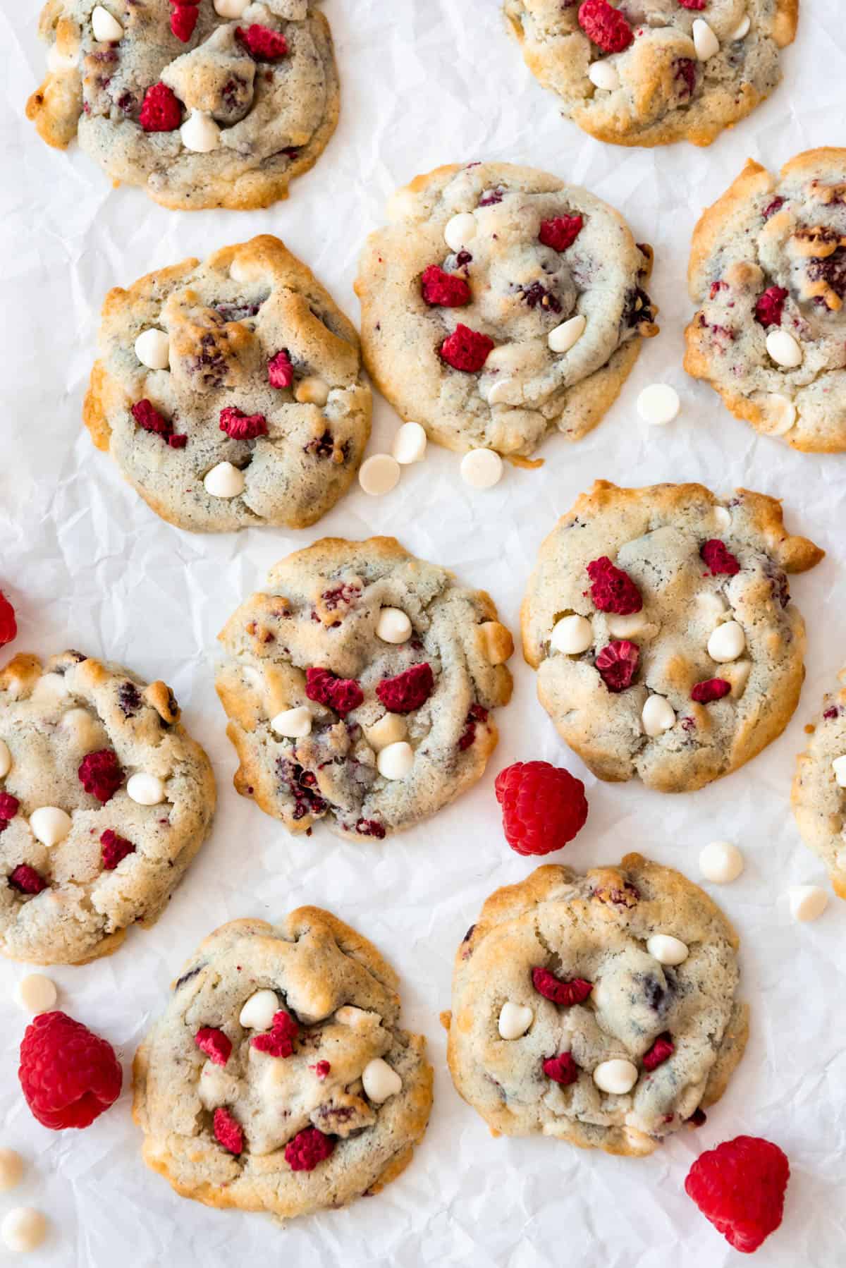 An overhead image of raspberry cheesecake cookies with scattered raspberries and white chocolate chips.