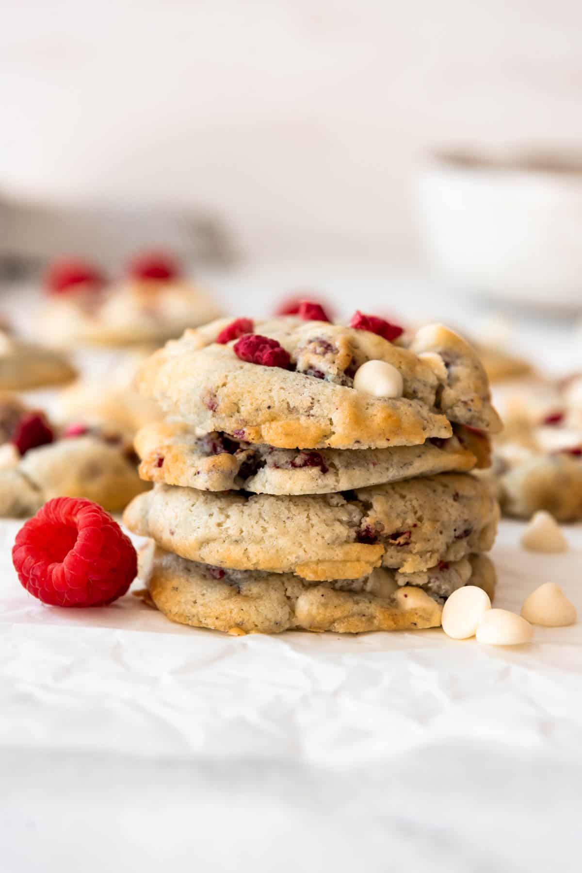 A stack of four raspberry cheesecake cookies with a fresh raspberry and white chocolate chips next to it.