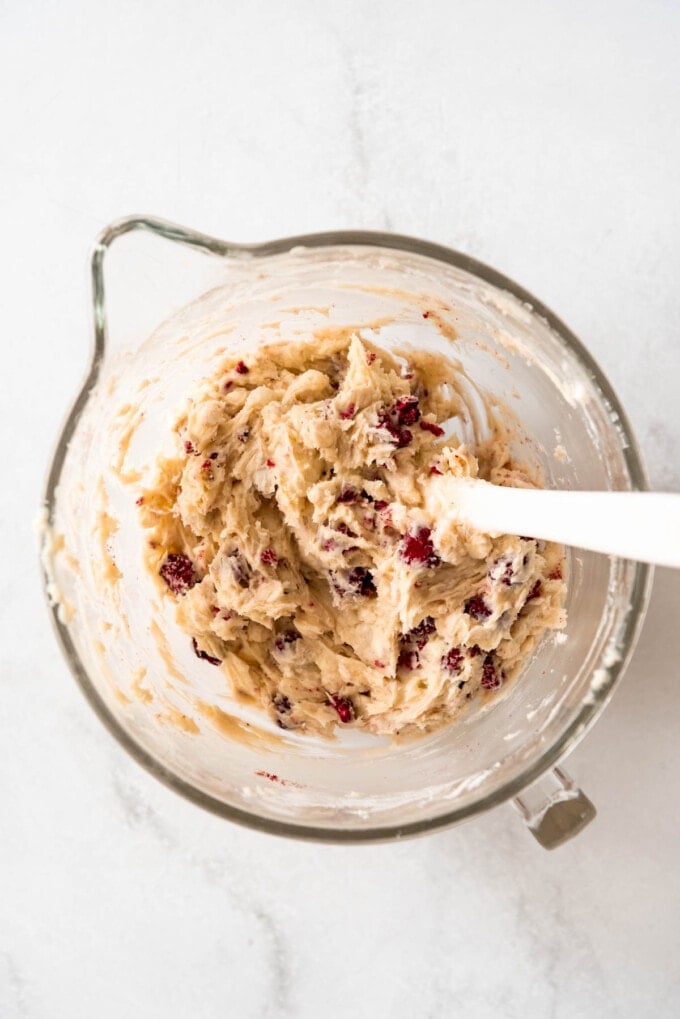 Stirring in freeze-dried raspberries and white chocolate chips into soft cookie dough with a white spatula.