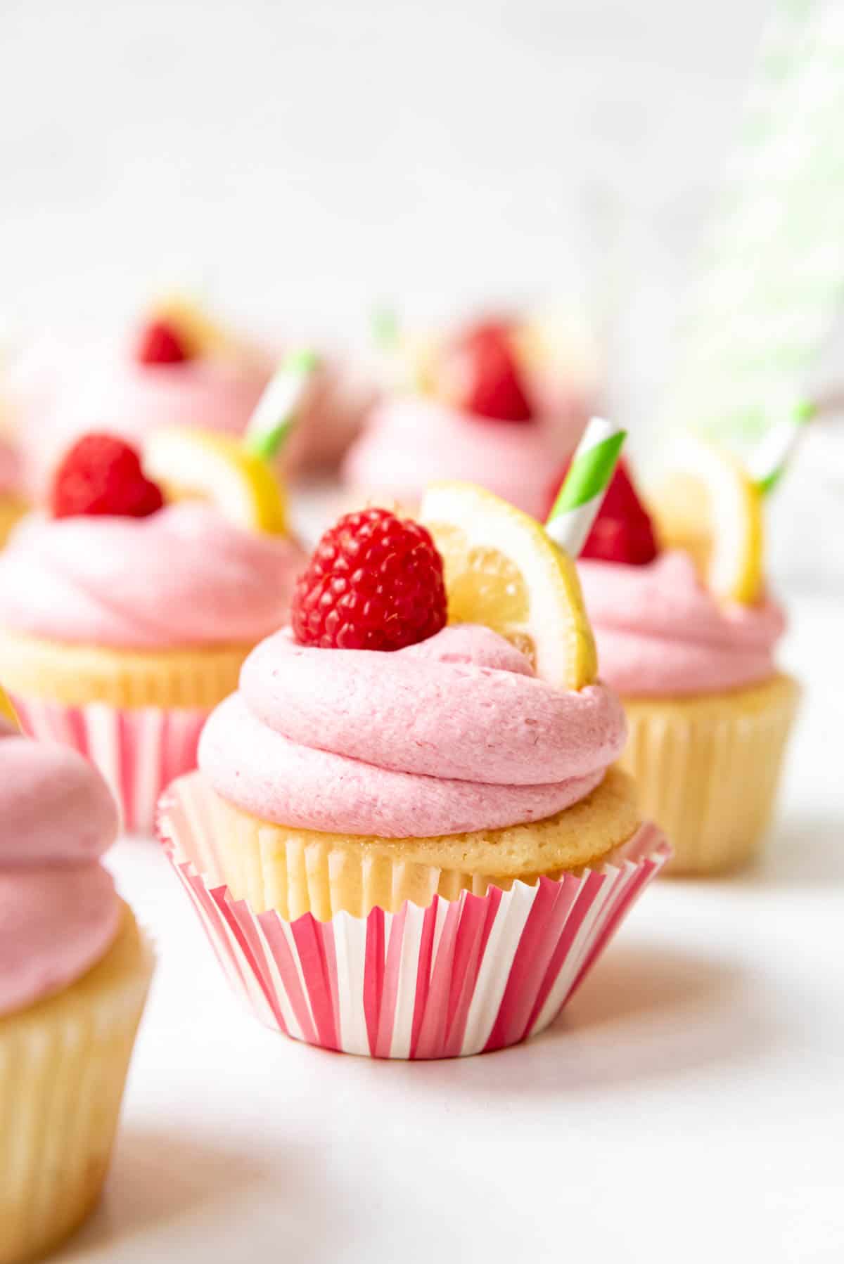 Raspberry lemonade cupcakes decorated with fresh raspberries, lemon slices, and straws.