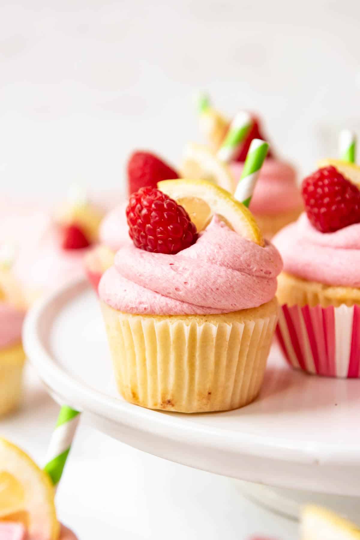 Raspberry lemonade cupcakes decorated with fresh raspberries, lemon slices, and straws.