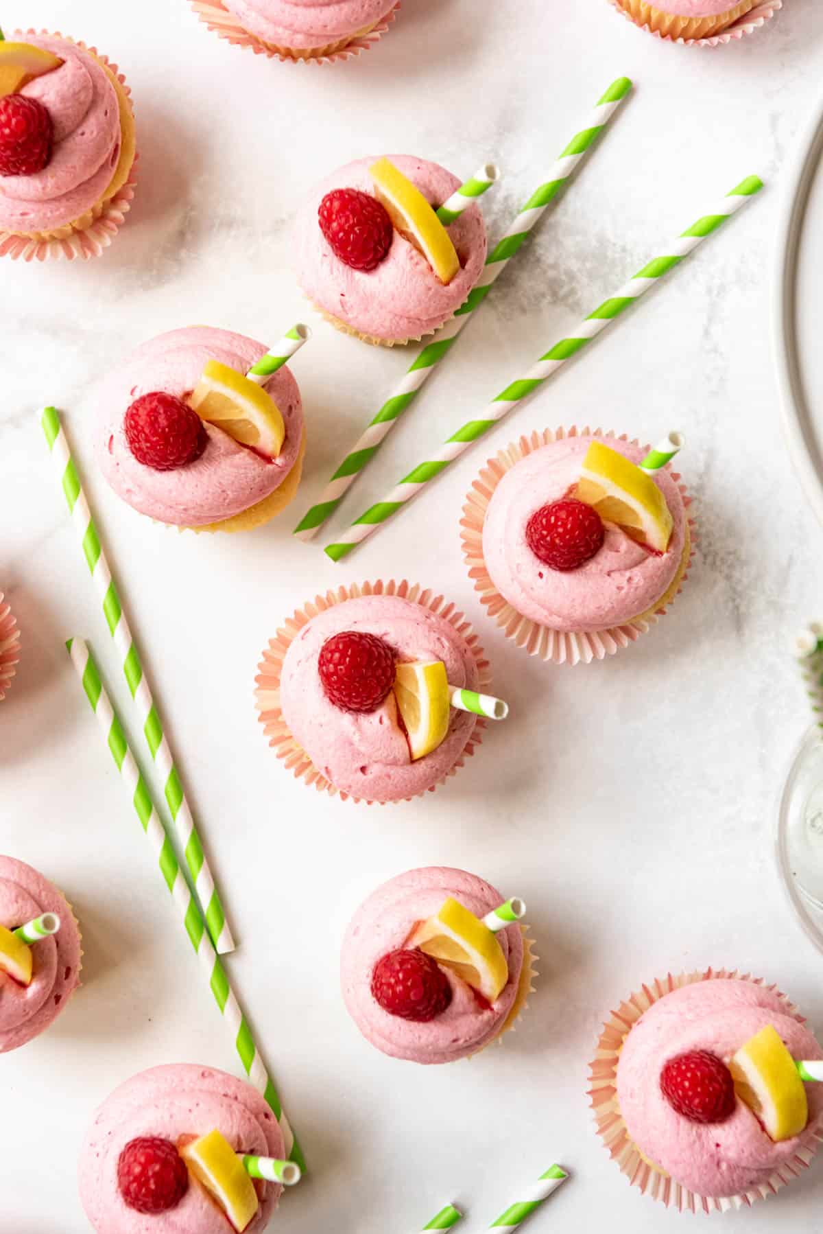 Top view of Raspberry lemonade cupcakes decorated with fresh raspberries, lemon slices, and straws.