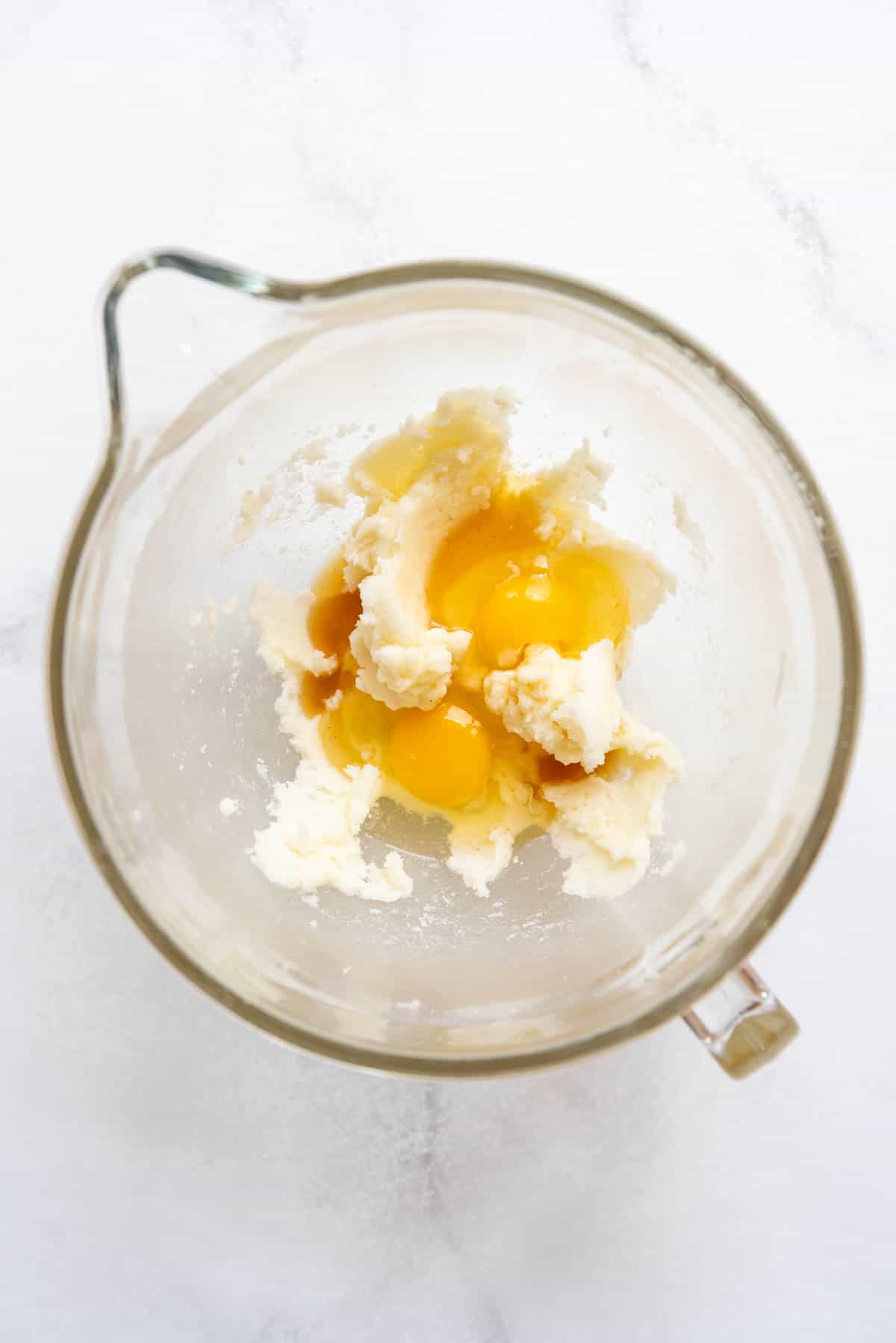 Top view of a glass mixing jug with creamed butter and sugar in it, and vanilla and eggs on top.