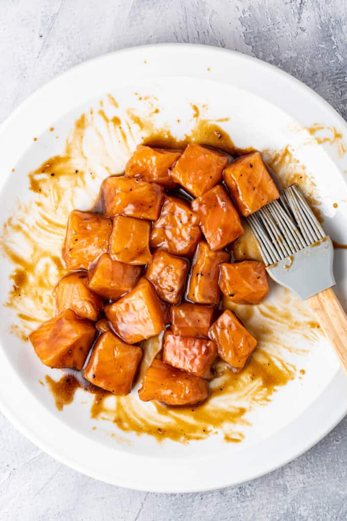 Bite-size pieces of cubed salmon brushed in glaze on a plate before cooking.