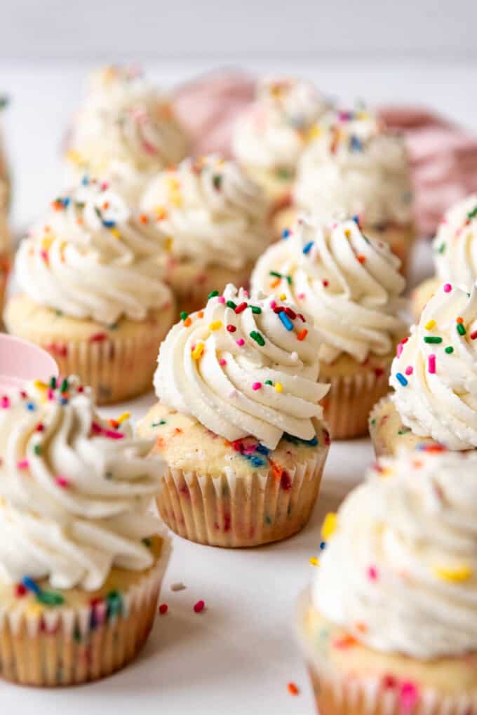 Frosted funfetti cupcakes in front of a pink linen napkin.