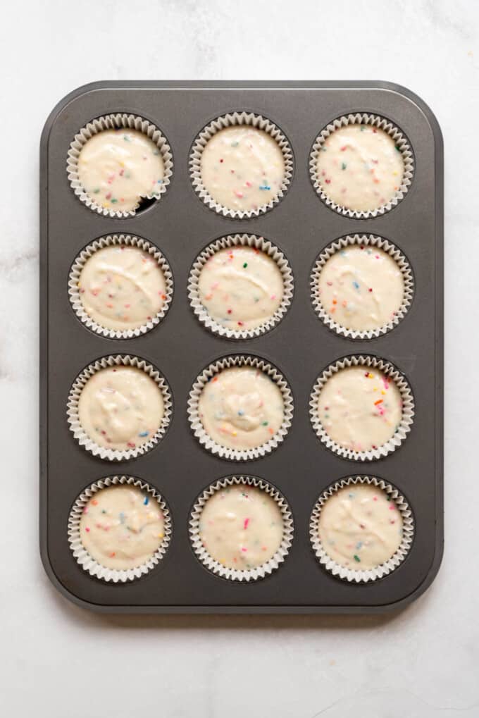 A muffin pan lined with cupcake liners filled with homemade funfetti cupcake batter.