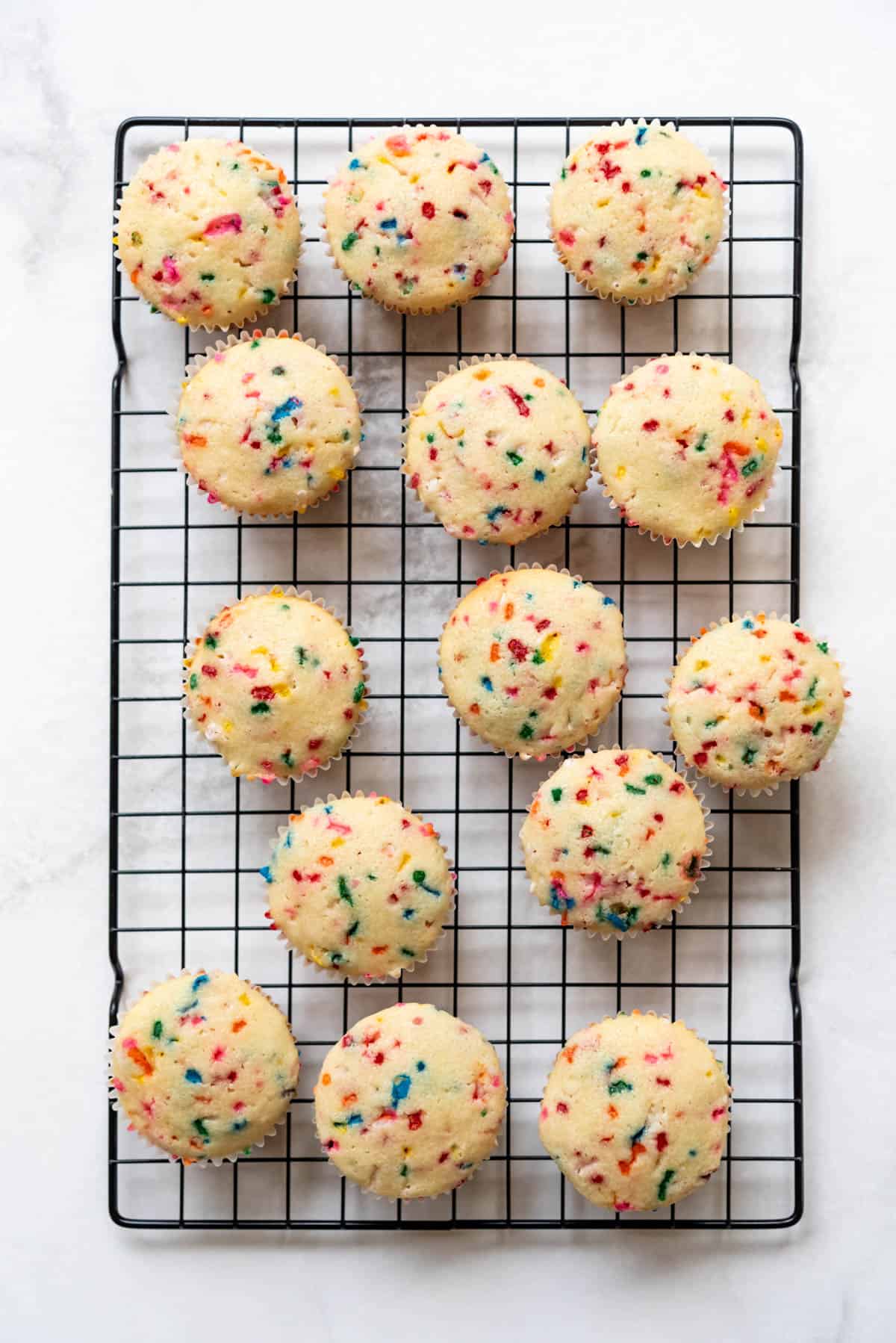 14 unfrosted homemade funfetti cupcakes on a wire cooling rack.
