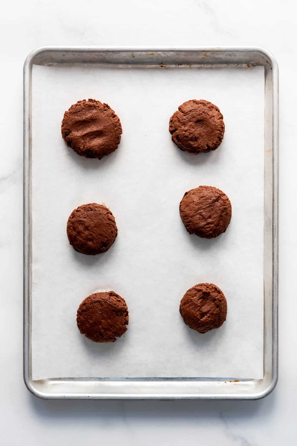 Balls of chocolate cookie dough that have been flattened slightly into pucks before baking.