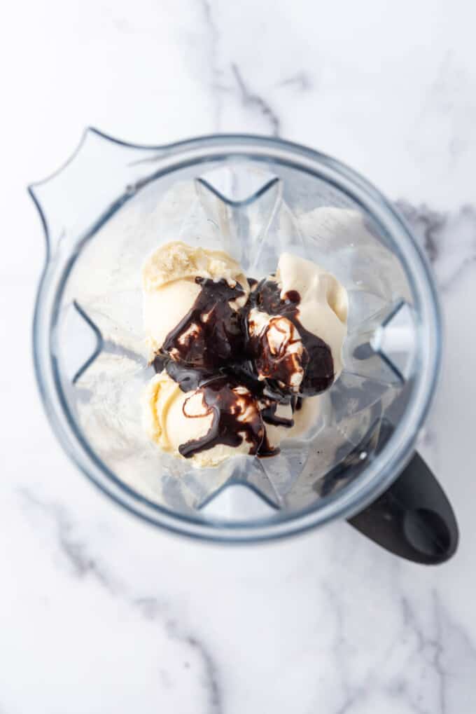 An image of chocolate sauce added to vanilla ice cream and milk in a blender.