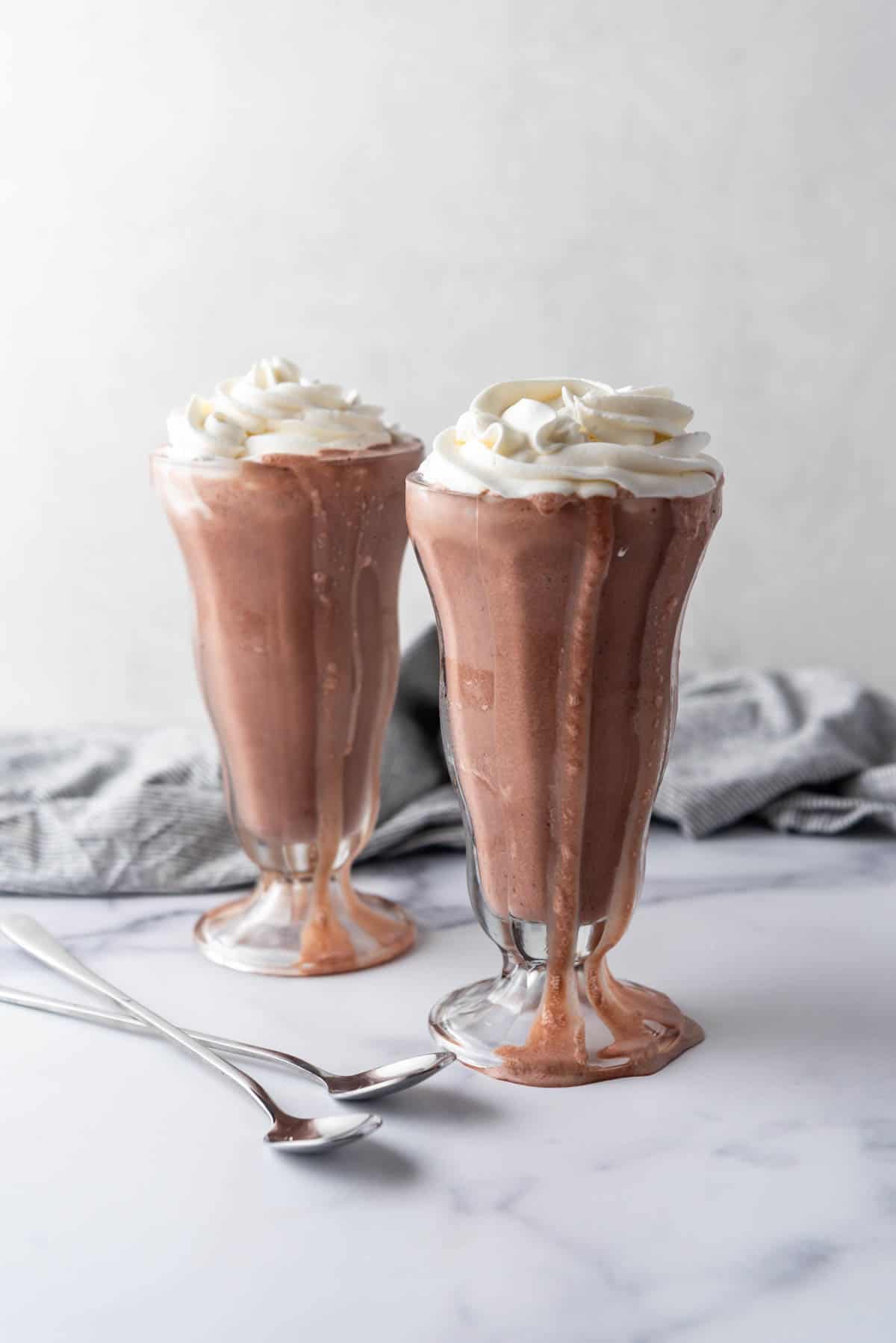 Two chocolate milkshakes with whipped cream on top.
