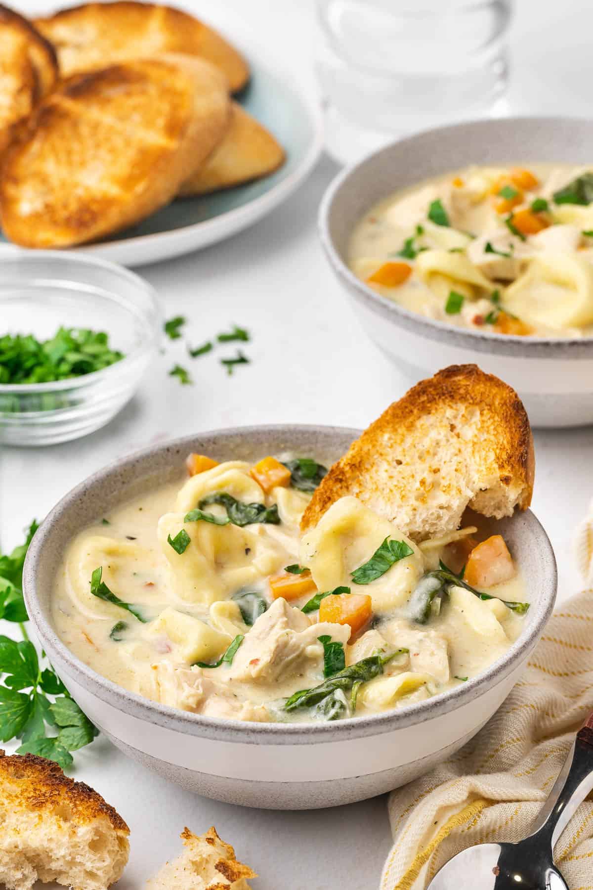 A bowl of creamy chicken tortellini soup with toasted bread in it.