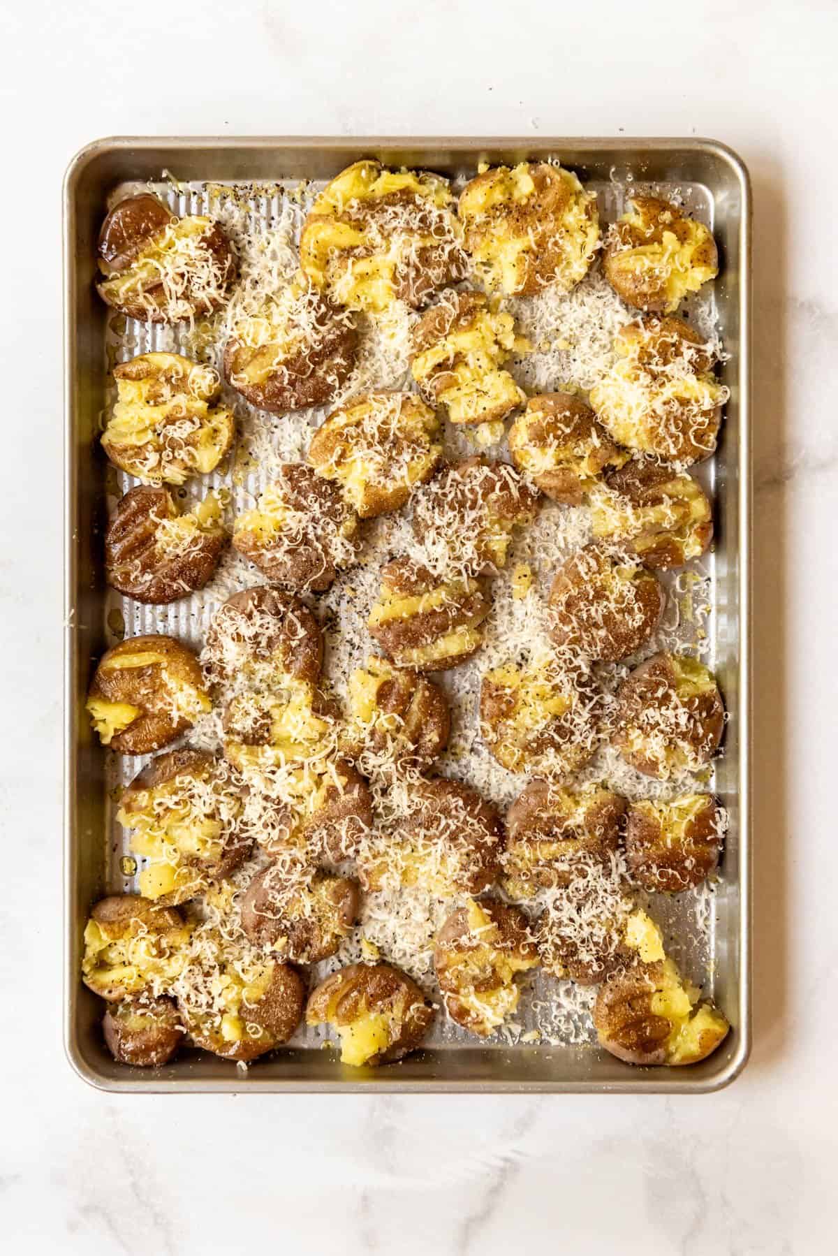 Parmesan cheese sprinkled over smashed potatoes on a baking sheet.