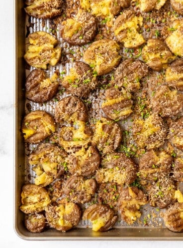 An image of crispy smashed potatoes with parmesan on a baking sheet.