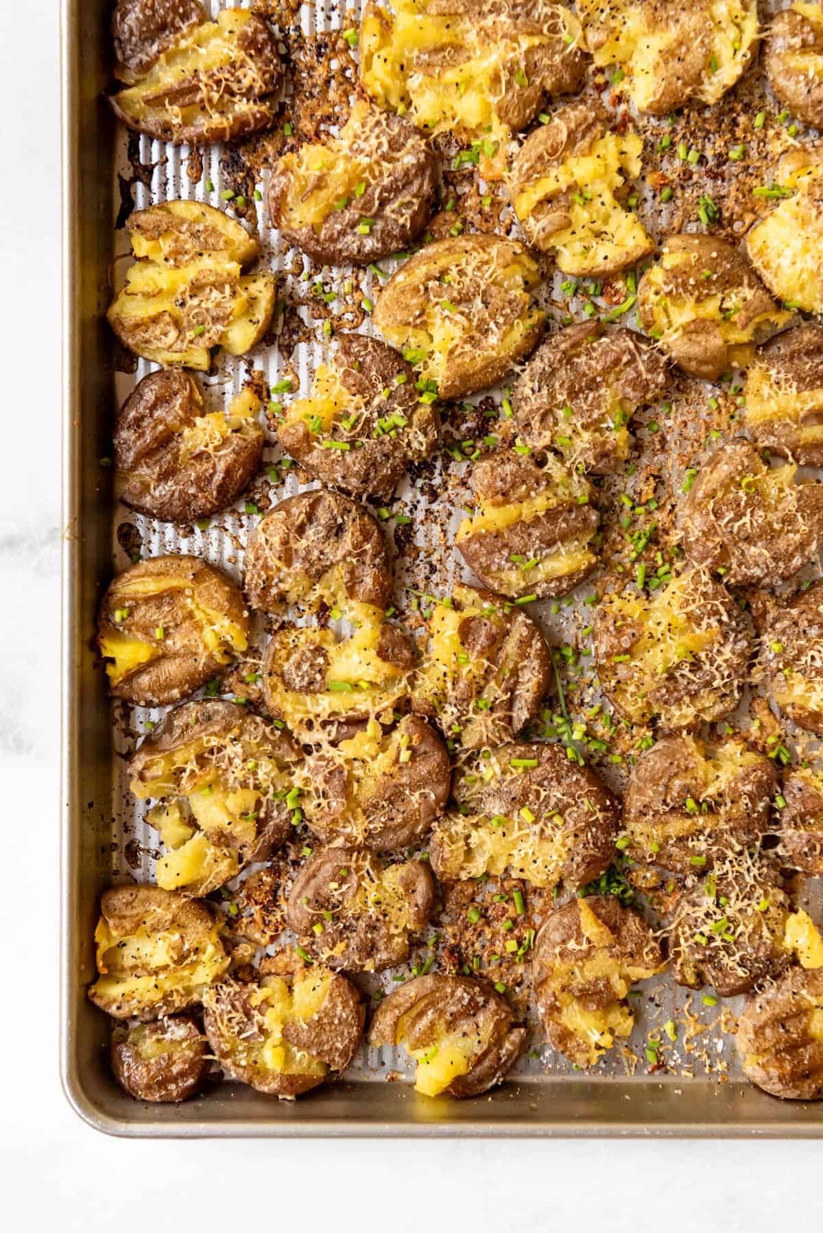 An image of crispy smashed potatoes with parmesan on a baking sheet.