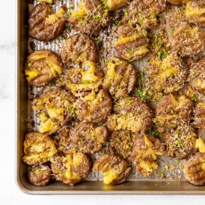 An image of crispy smashed potatoes with parmesan on a baking sheet.