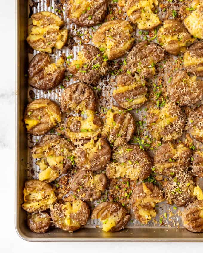 An image of crispy smashed potatoes with parmesan on a baking sheet.