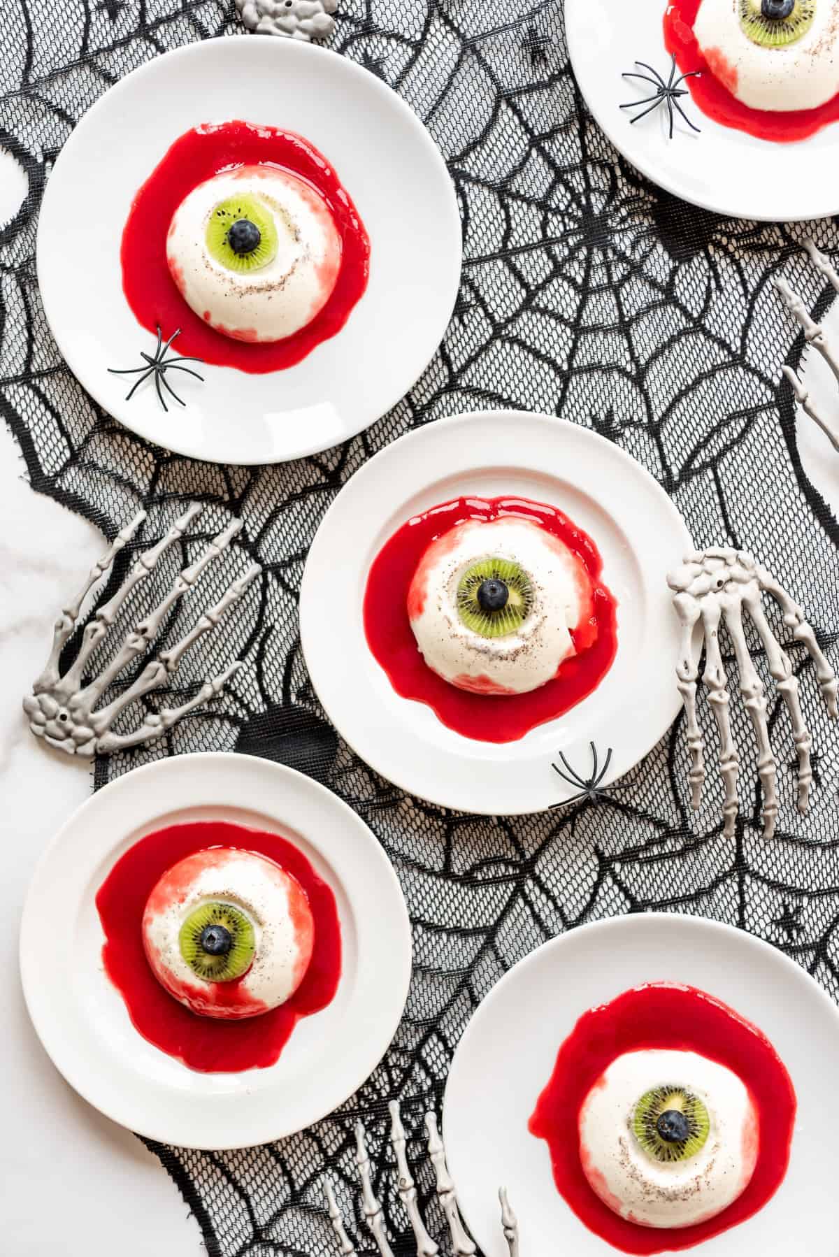 An image of panna cotta eyeballs made of kiwis and blueberries surrounded by Halloween decor.