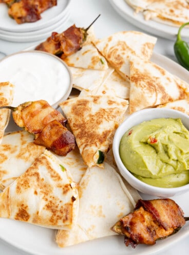 Jalapeno popper quesadillas on a plate with bacon wrapped jalapeno poppers.