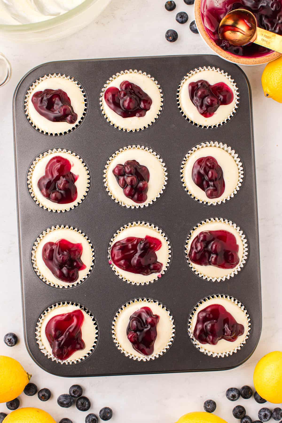 Adding dollops of blueberry pie filling to mini cheesecakes in a cupcake pan.