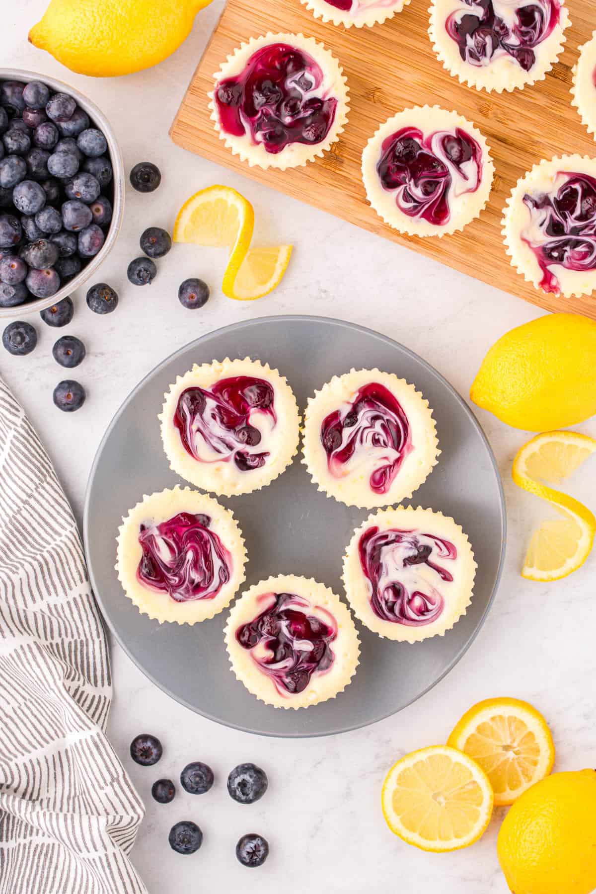 An overhead image of mini lemon blueberry cheesecakes with blueberries and lemons scattered around.
